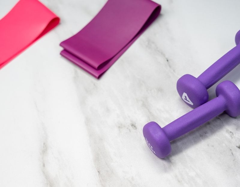 flat lay of pastel pink fitness gear including sneakers and dumbbells on marble texture