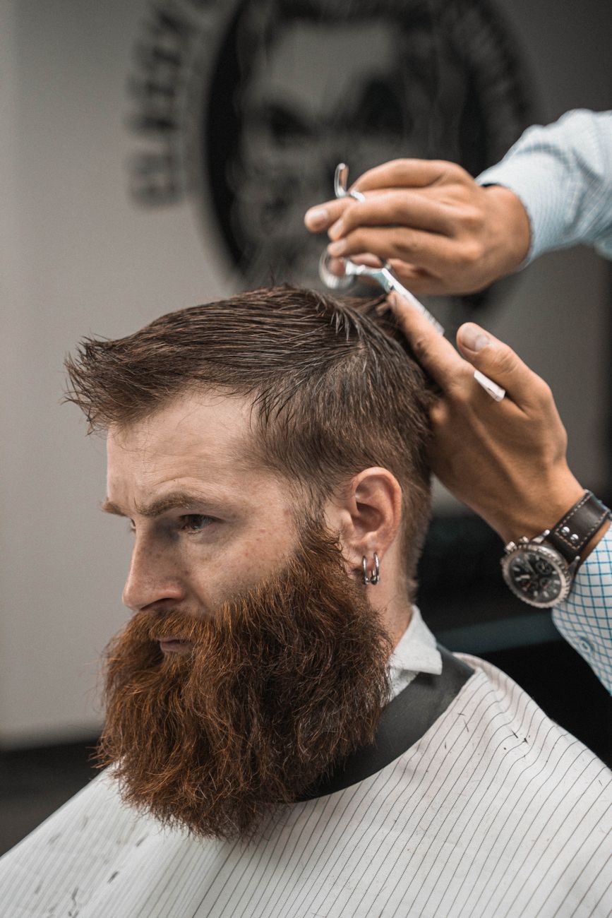 gros plan sur un barber coiffant les cheveux d un homme barbu a l interieur vue de cote capturant le processus de coupe de cheveux precis