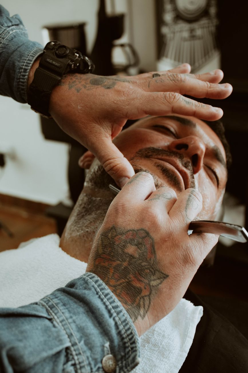 gros plan sur un barbier tatoue rasant habilement le visage d un client dans un salon de coiffure moderne
