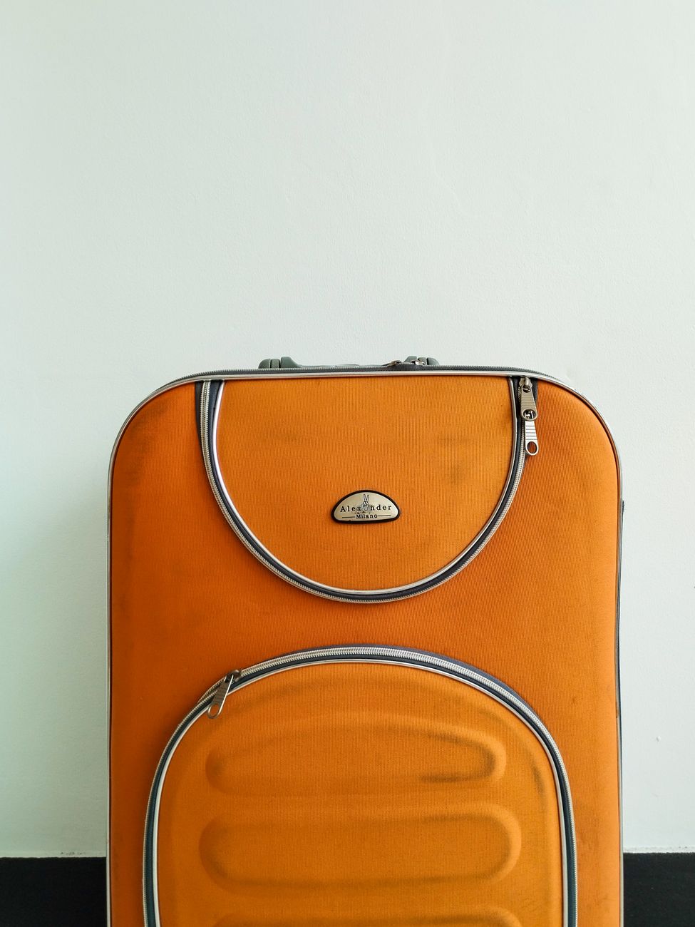 gros plan sur une valise orange avec des accents metalliques contre un mur uni