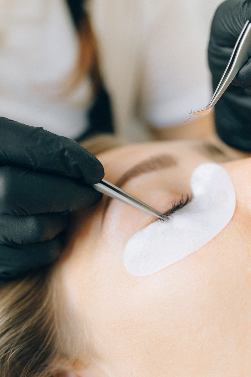 technicienne en gants noirs appliquant des extensions de cils sur l oeil d une femme dans un salon de beaute
