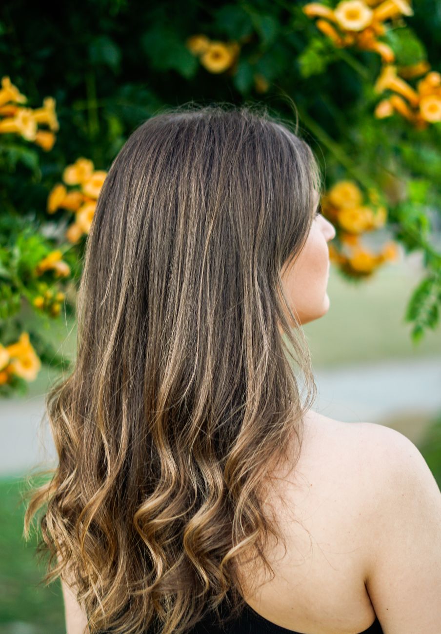 vue de dos d une femme aux cheveux longs et fluides se tenant sous un arbre avec des fleurs orange vives