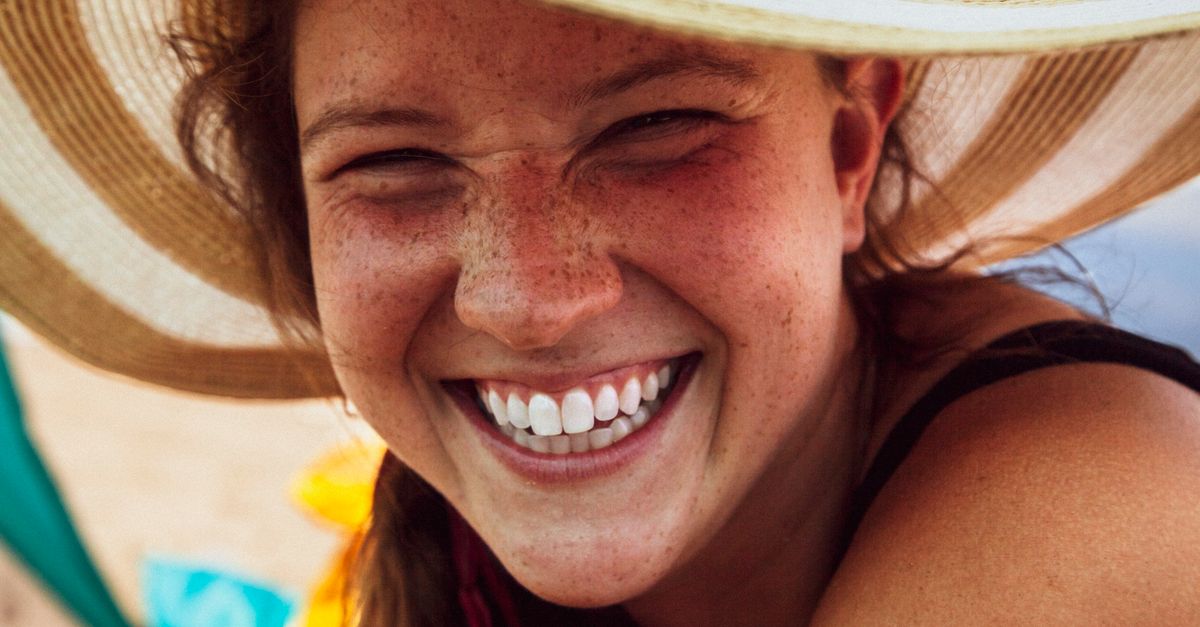 gros plan d une femme souriante avec des taches de rousseur portant un chapeau de soleil degageant de la joie