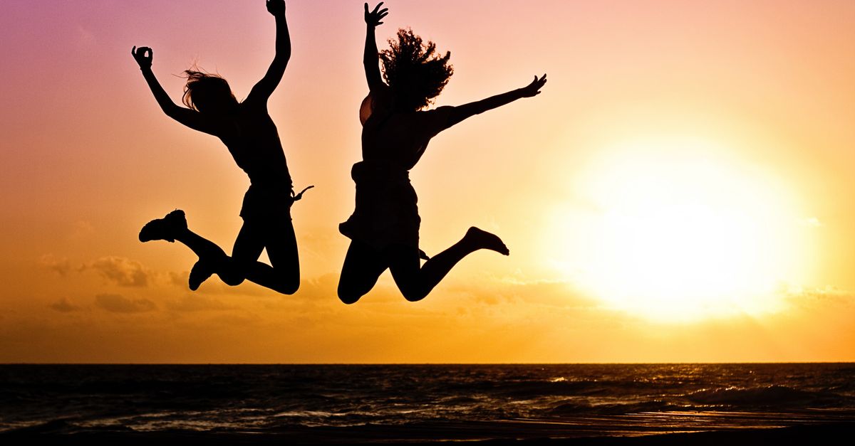 silhouettes de deux personnes sautant joyeusement sur une plage lors d un coucher de soleil vibrant
