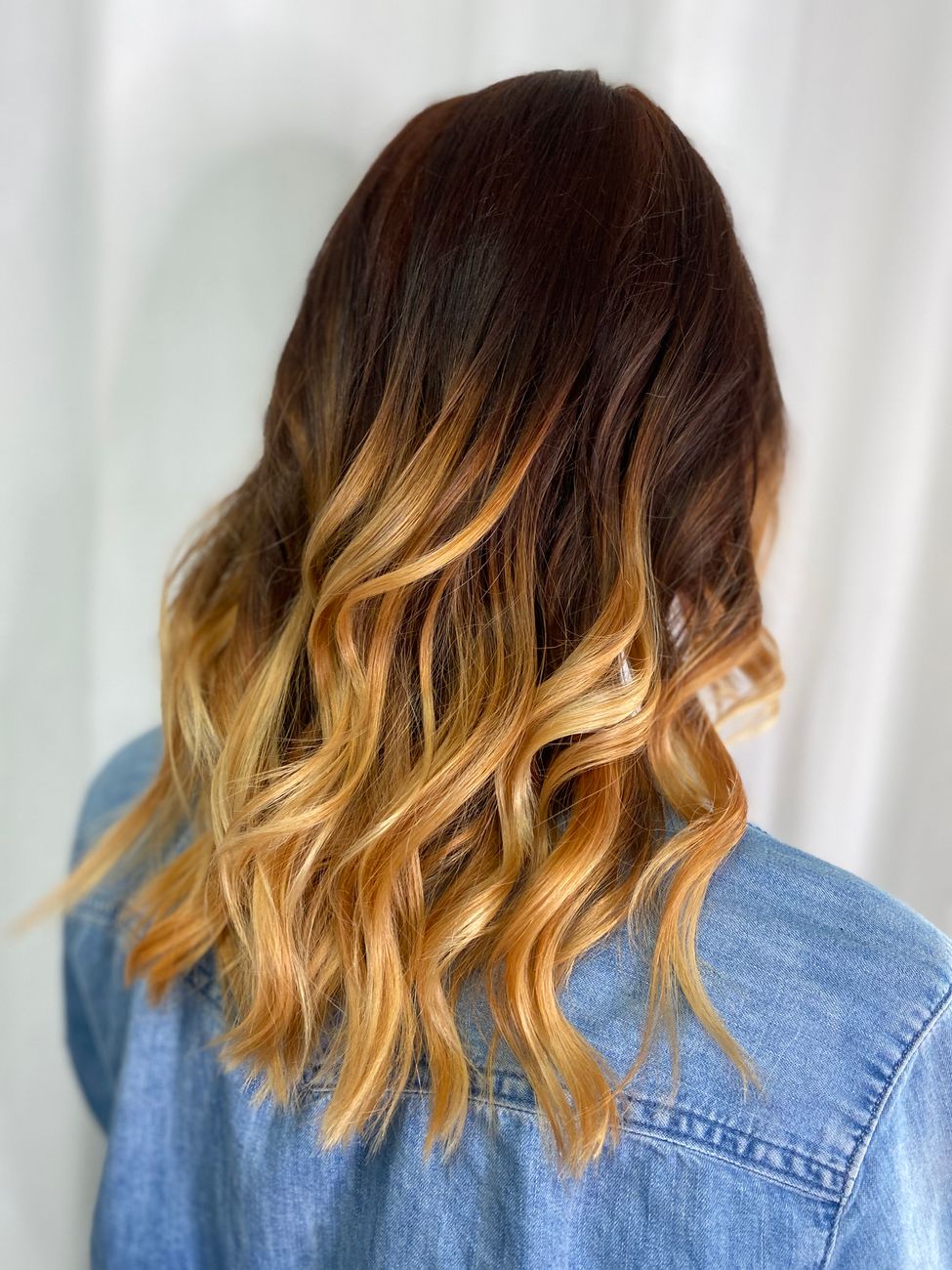 une femme mettant en valeur de magnifiques cheveux boucles ombres portant une veste en jean