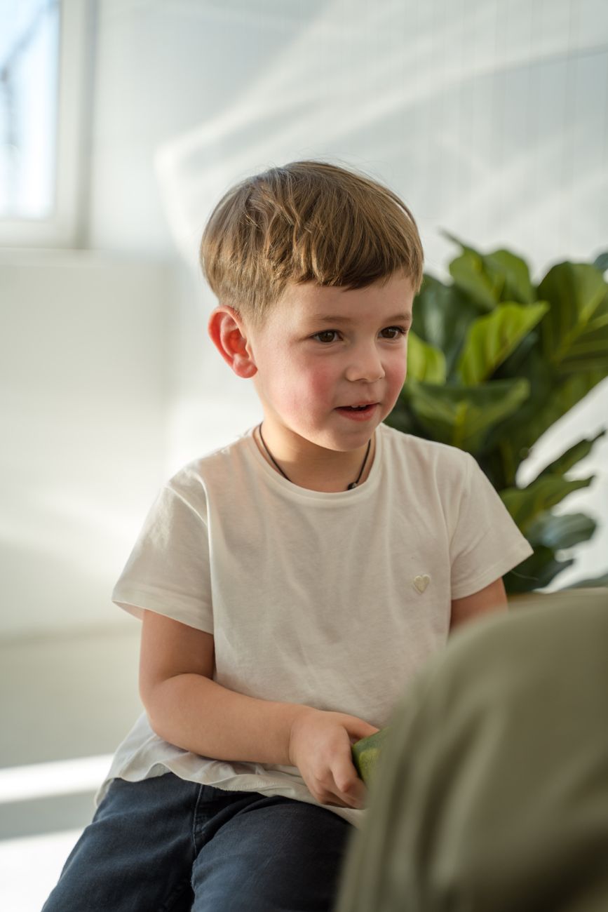 portrait d un jeune garcon souriant a l interieur avec de la lumiere naturelle et des plantes vertes en arriere plan