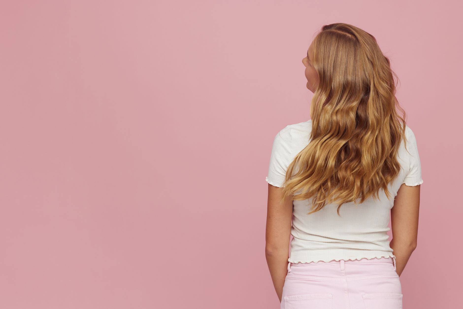vue arriere d une femme avec de longs cheveux ondules blonds sur un arriere plan rose