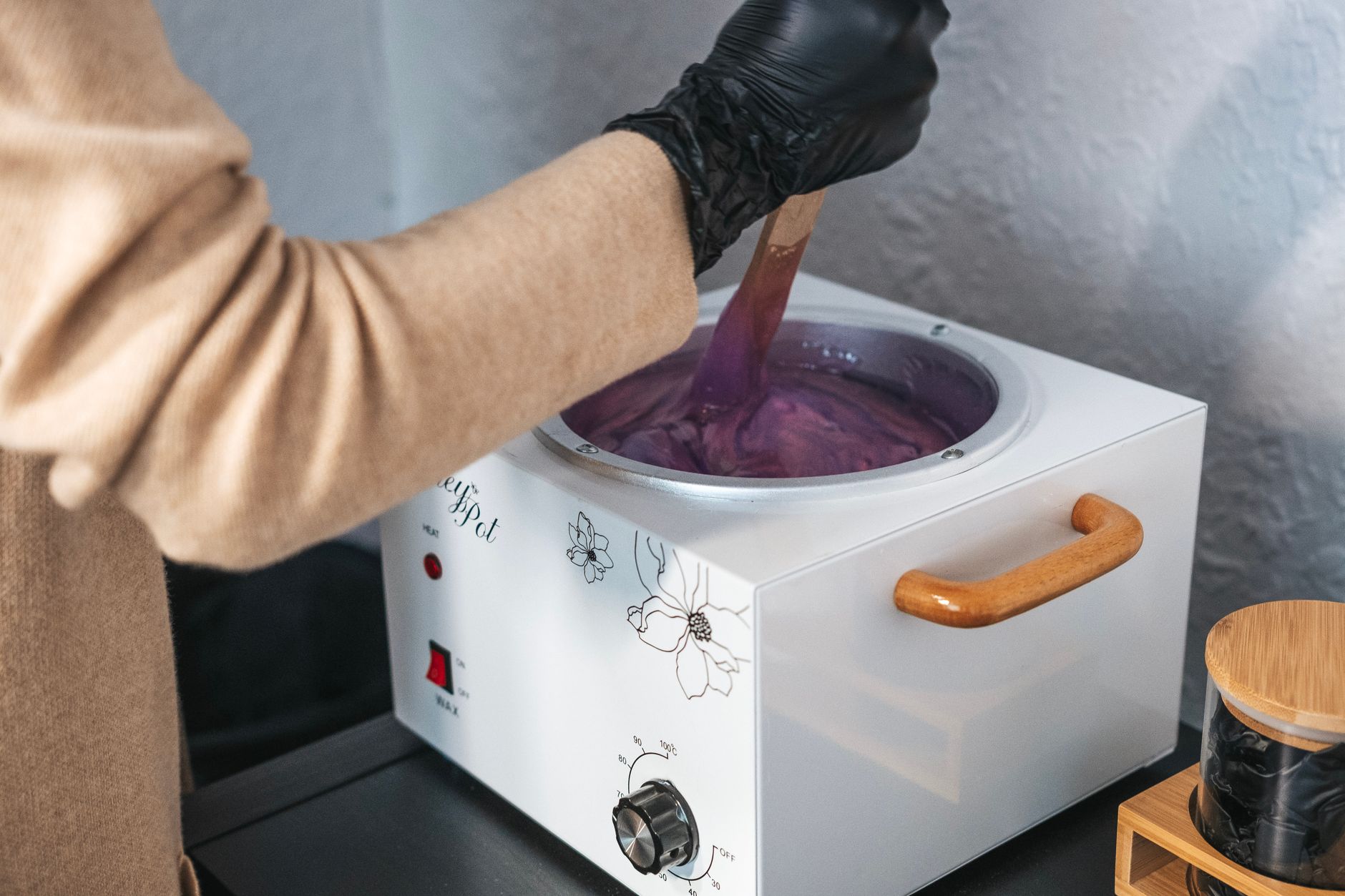une estheticienne portant des gants remuant de la cire violette dans un pot a cire a l interieur