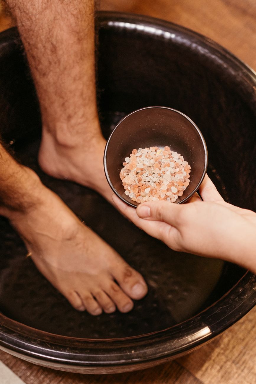 gros plan sur un bain de pieds avec des sels de bain roses tenus au dessus offrant relaxation