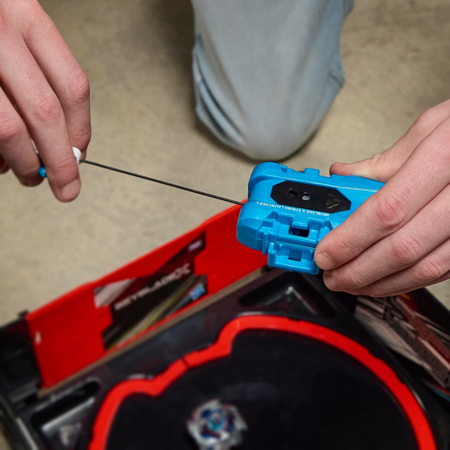 Joueur qui tire la corde du lanceur au-dessus dune arène Beyblade X, vendue à part