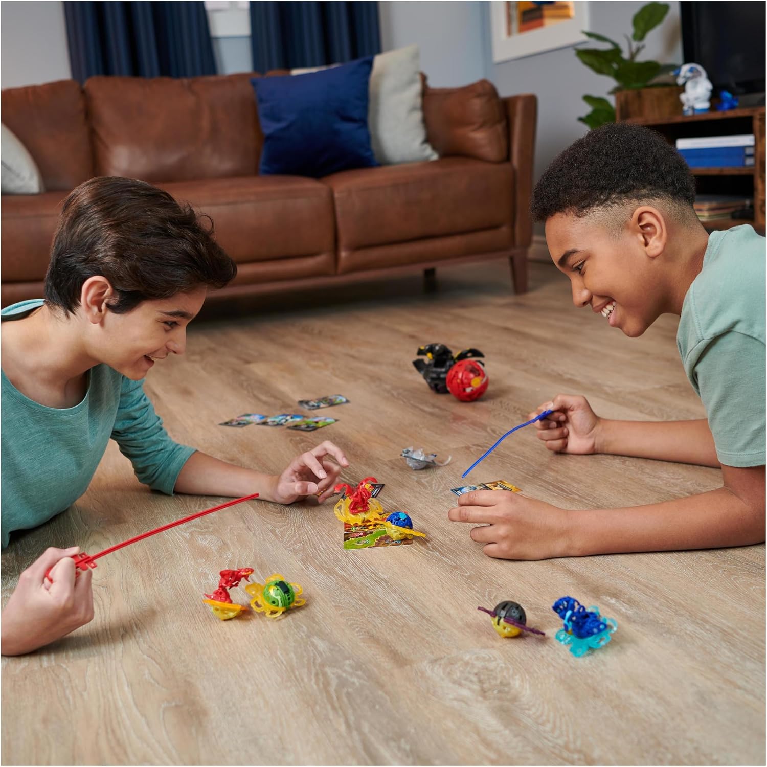 Deux enfants lancent leurs Bakugan sur un parquet, cartes étalées autour deux