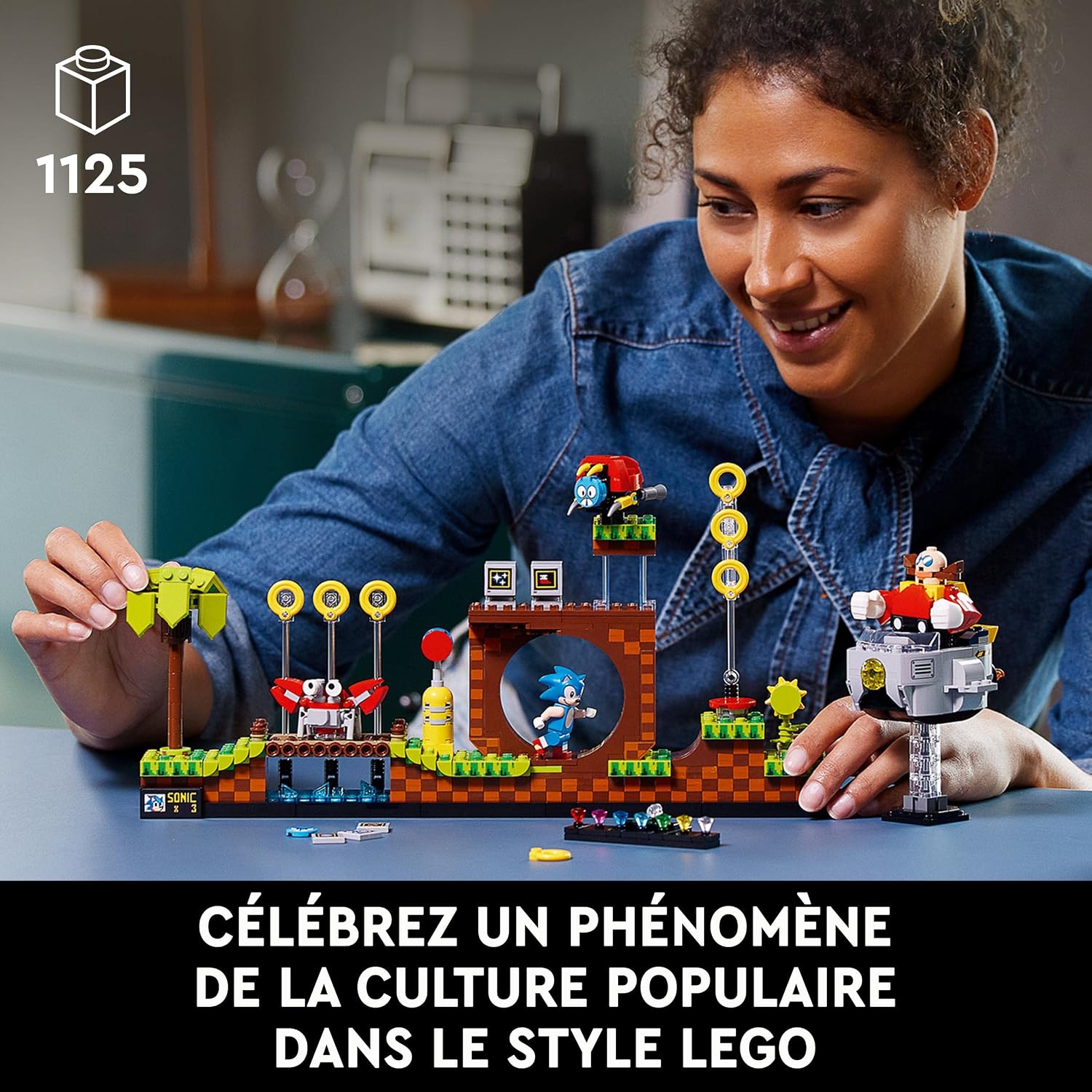 Femme souriante qui construit la Green Hill Zone LEGO sur une table, pastille 1125 pièces, légende en français