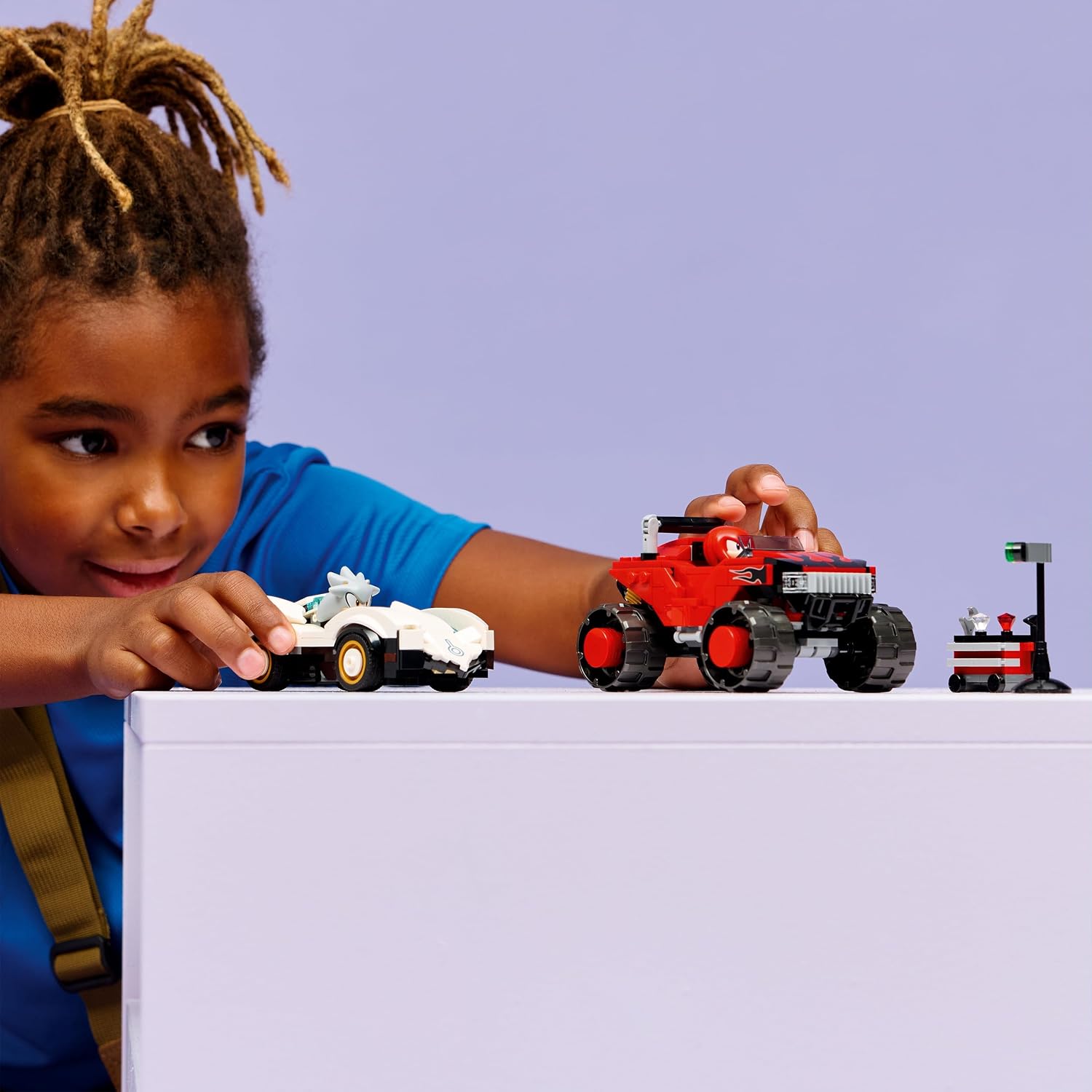 Enfant qui fait rouler les deux véhicules LEGO sur une table, le feu de départ à côté