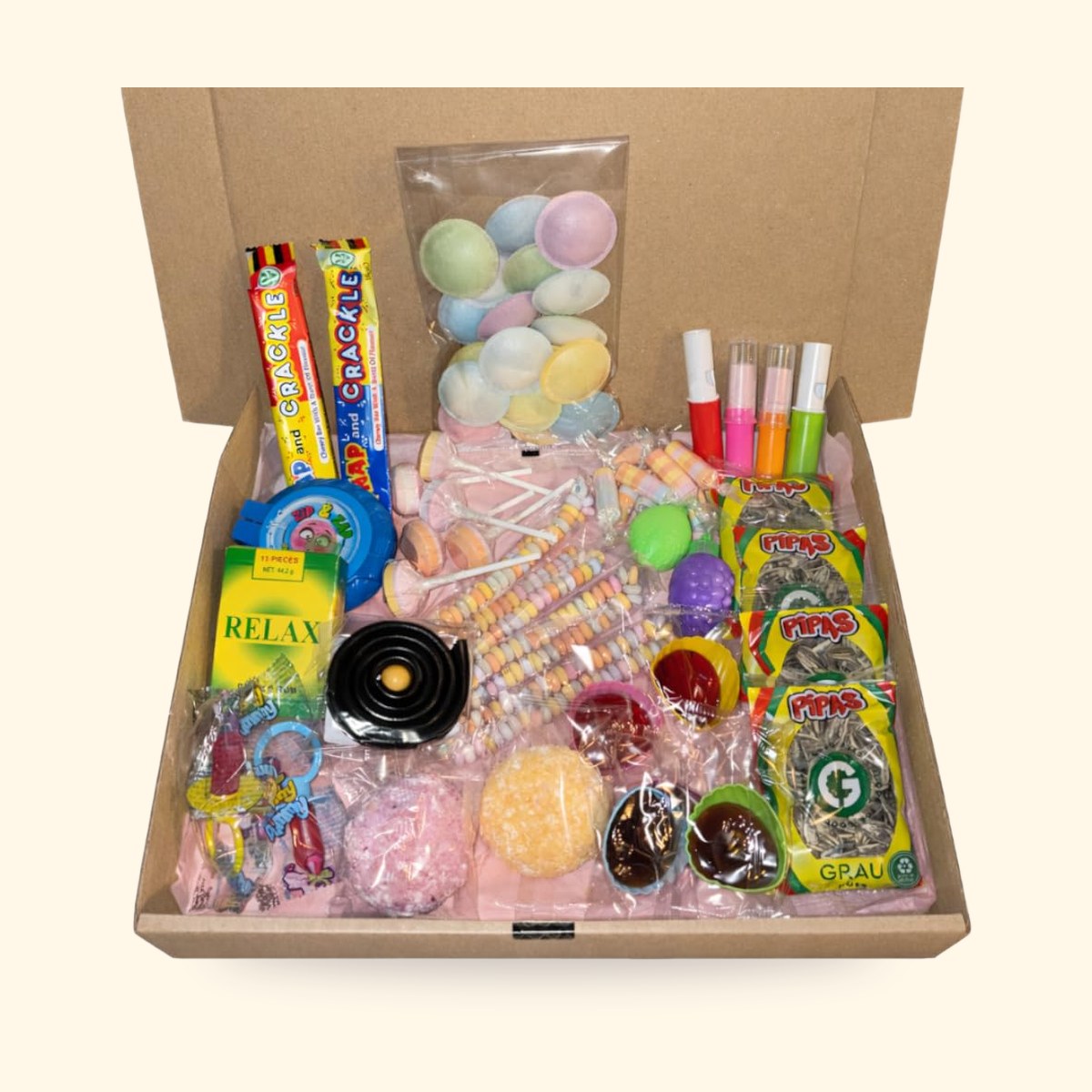 Box en carton ouverte garnie de bonbons rétro : soucoupes, colliers, sucettes, roudoudous, sur fond crème