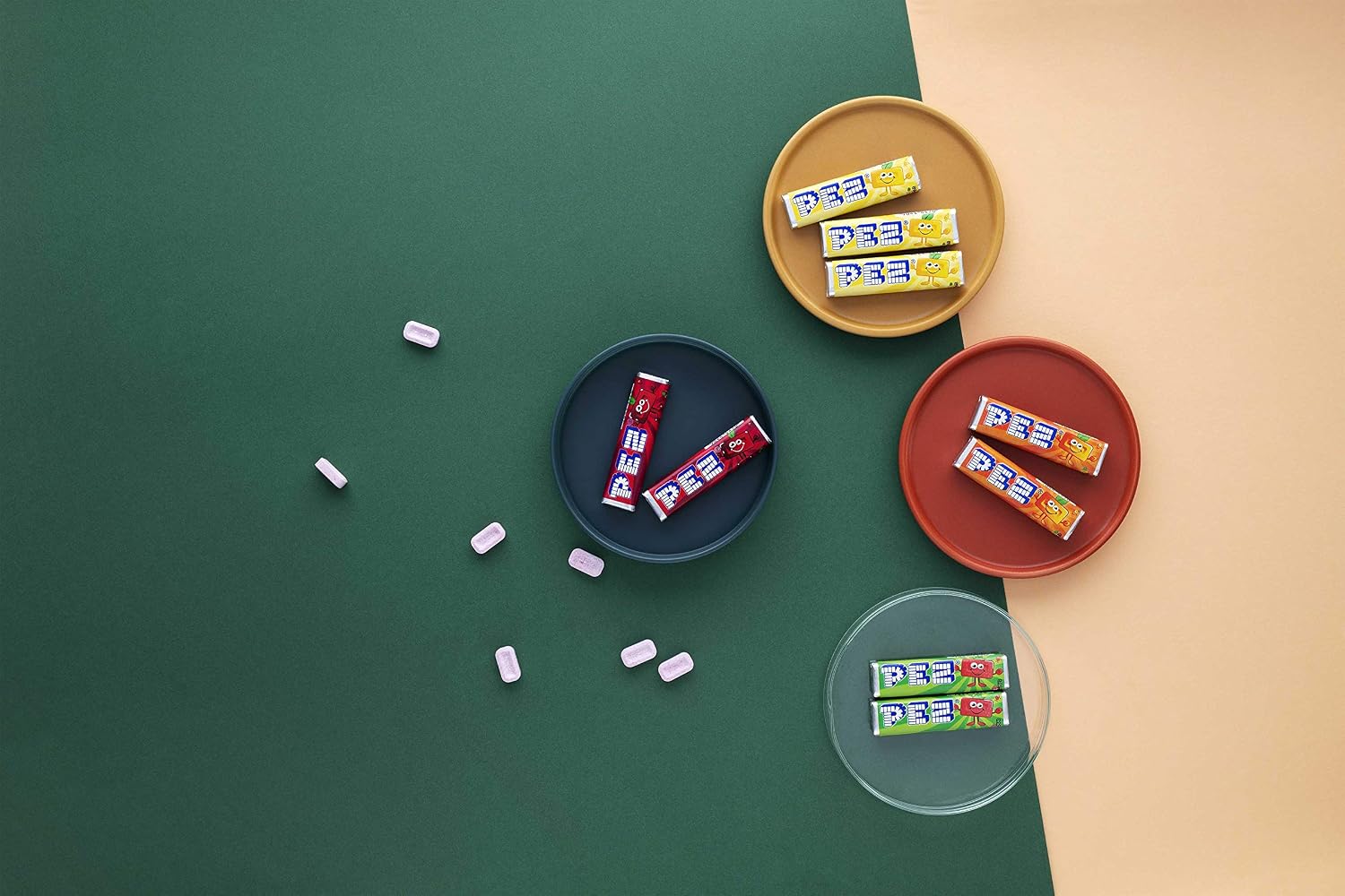 Visuel publicitaire : recharges PEZ dans des coupelles et bonbons épars sur fond vert