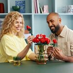 Deux adultes composent le bouquet de roses LEGO dans un vase en verre