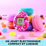 Tamagotchi Berry Delicious posé devant des macarons et des bonbons colorés
