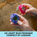 Deux mains tenant le Tama Universe et un Tamagotchi rose au-dessus dune table en bois