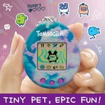 Tamagotchi Original Sky tenu entre deux doigts, visuel publicitaire en anglais