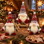 Trois gnomes de Noël en peluche aux bonnets tricotés avec leurs luges sur une table près de biscuits en pain d'épices