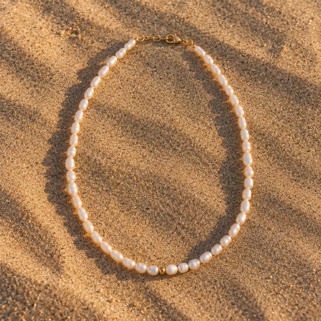 Collier de perles d’eau douce baroques blanches posé sur le sable au coucher du soleil