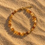 Bracelet en perles de verre miel et ambre posé sur le sable au coucher du soleil