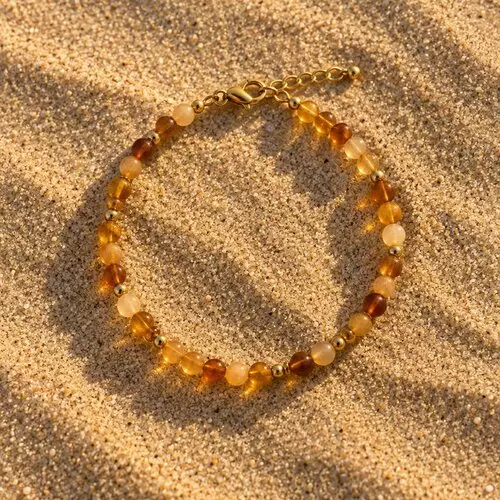 Bracelet en perles de verre miel et ambre posé sur le sable au coucher du soleil