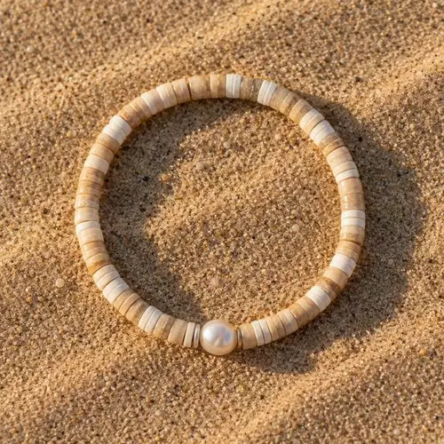 Bracelet en perles heishi couleur sable avec une perle d’eau douce posé sur le sable