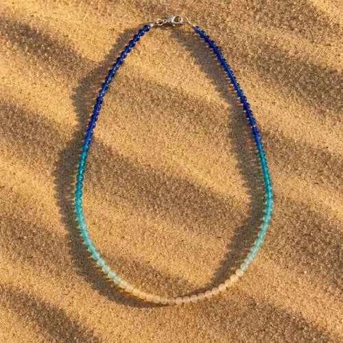 Collier en perles de verre en dégradé bleu océan et sable posé sur le sable