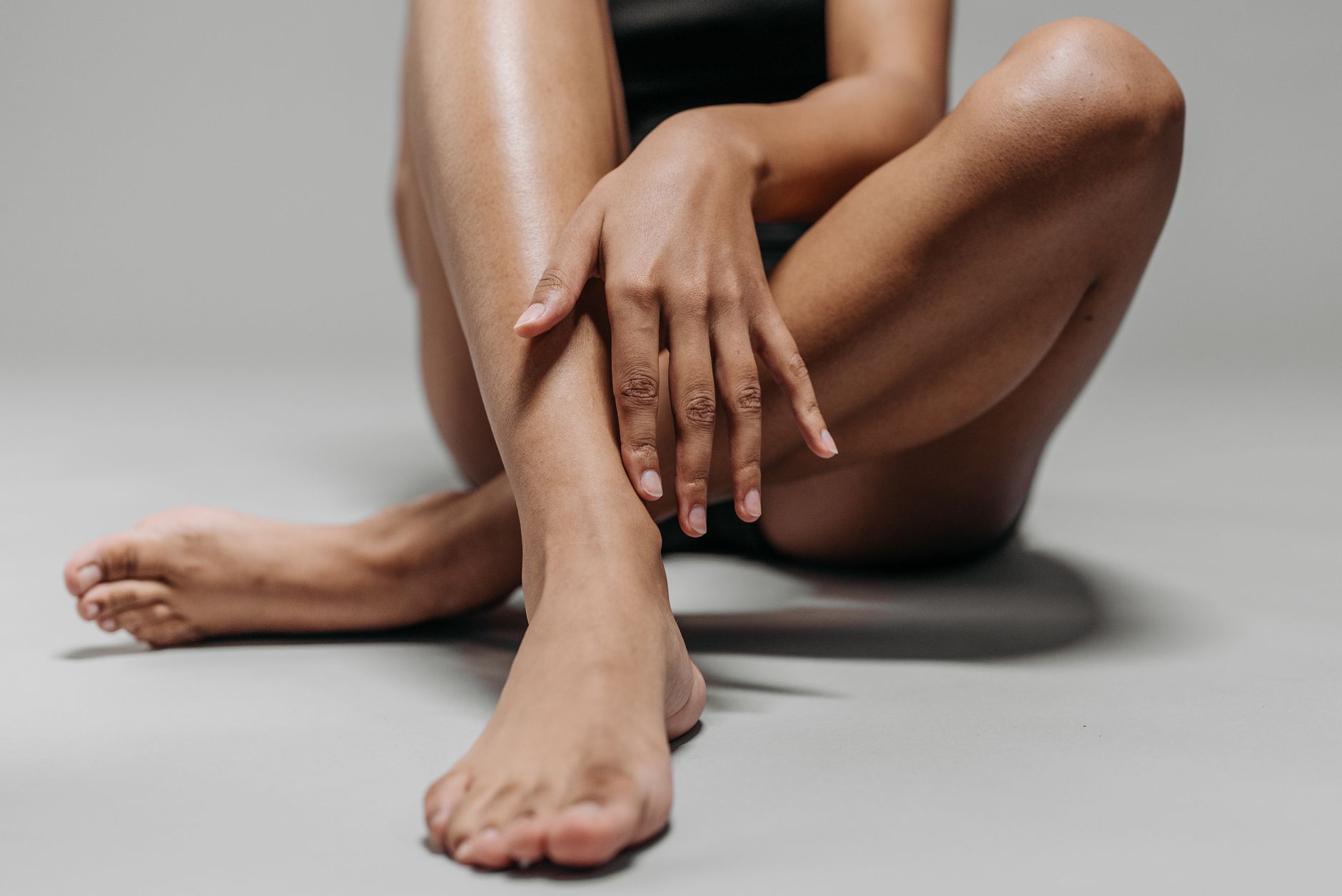 vue rapprochee des jambes et des mains d une femme assise en tailleur sur le sol mettant en valeur le teint et la texture de la peau