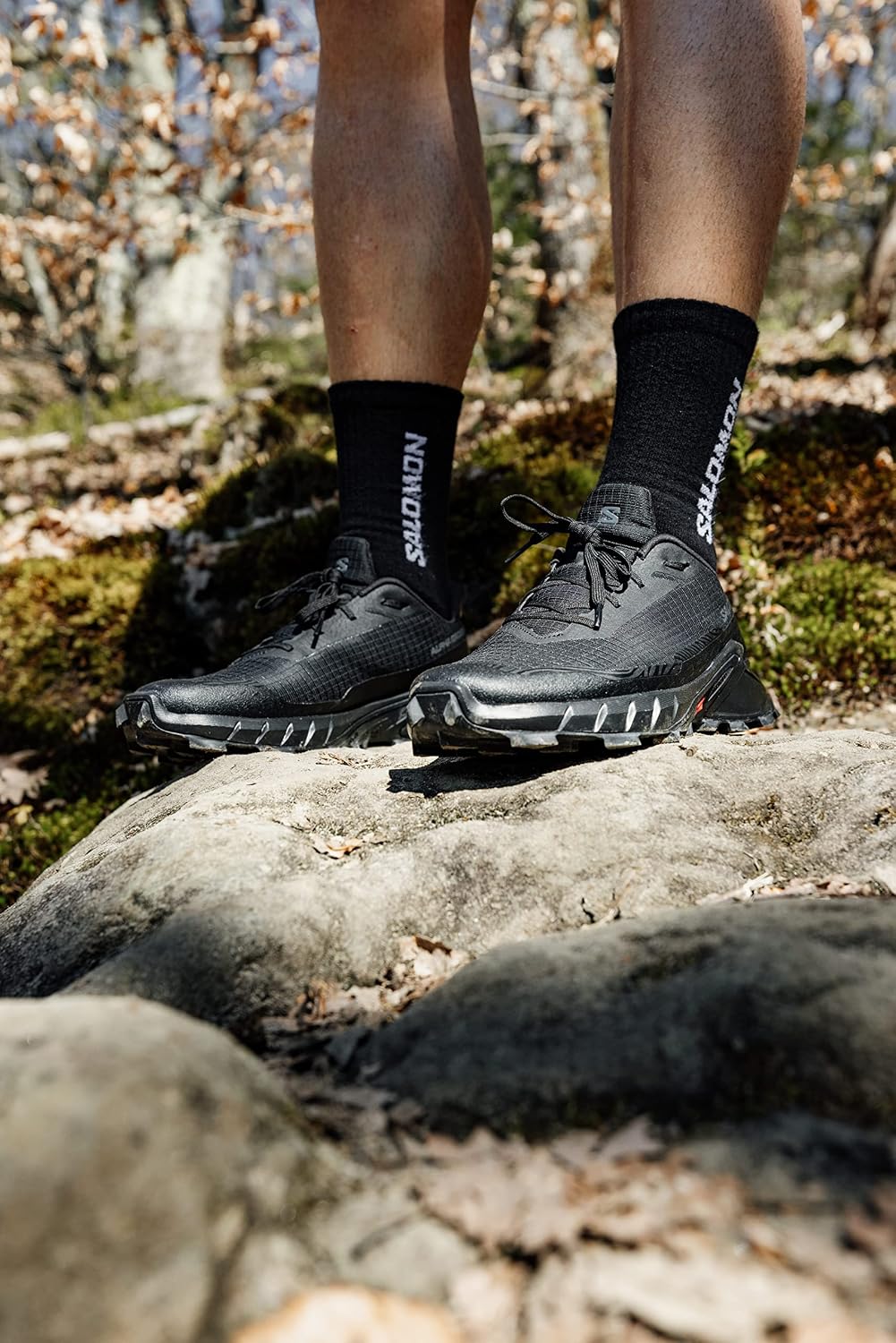 Runner con Salomon Alphacross 5 nere in piedi su una roccia nel bosco