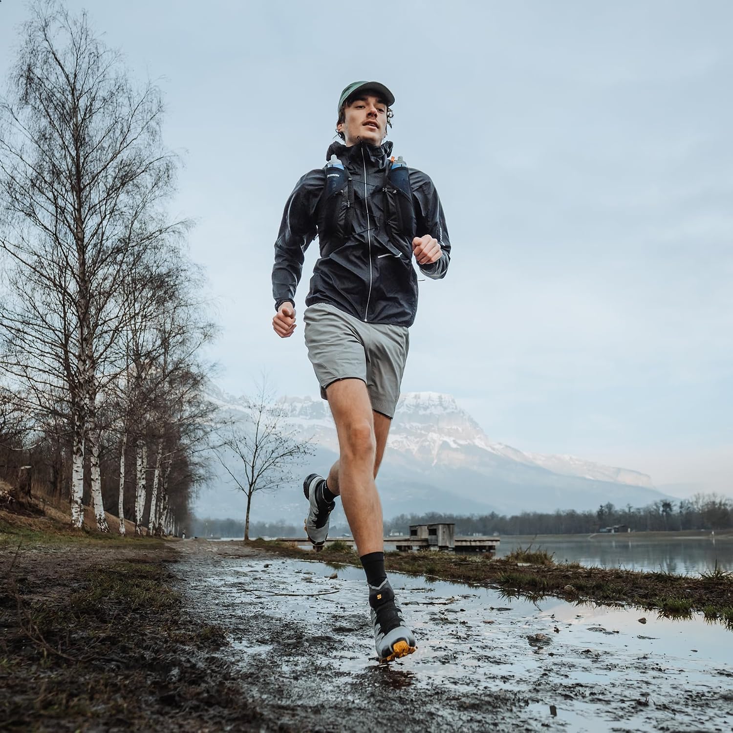 Runner con giacca nera corre su un sentiero fangoso vicino a un lago
