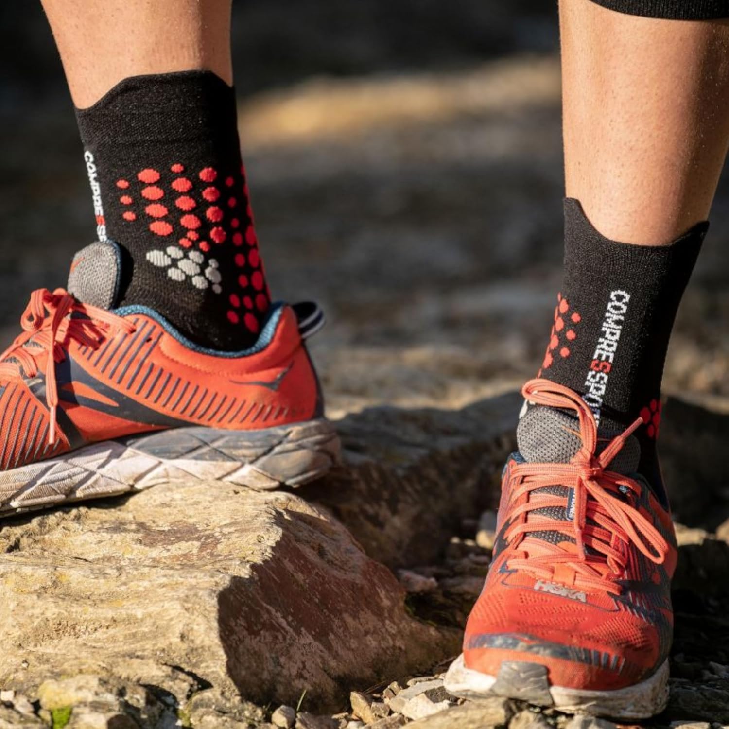 Calza Compressport nera e rossa indossata con scarpa da trail su roccia
