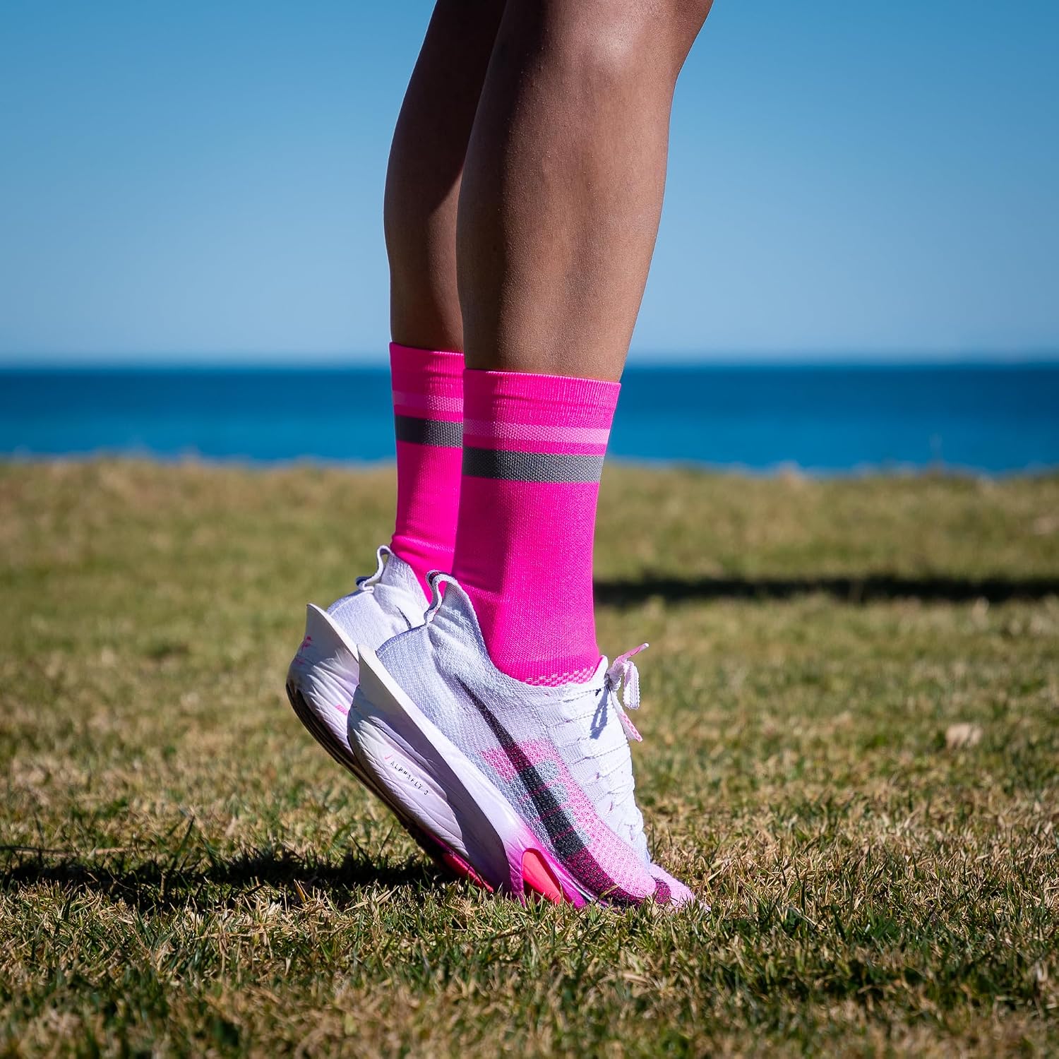 Calze NORTEI rosa fluo indossate con scarpe da corsa su un prato in riva al mare