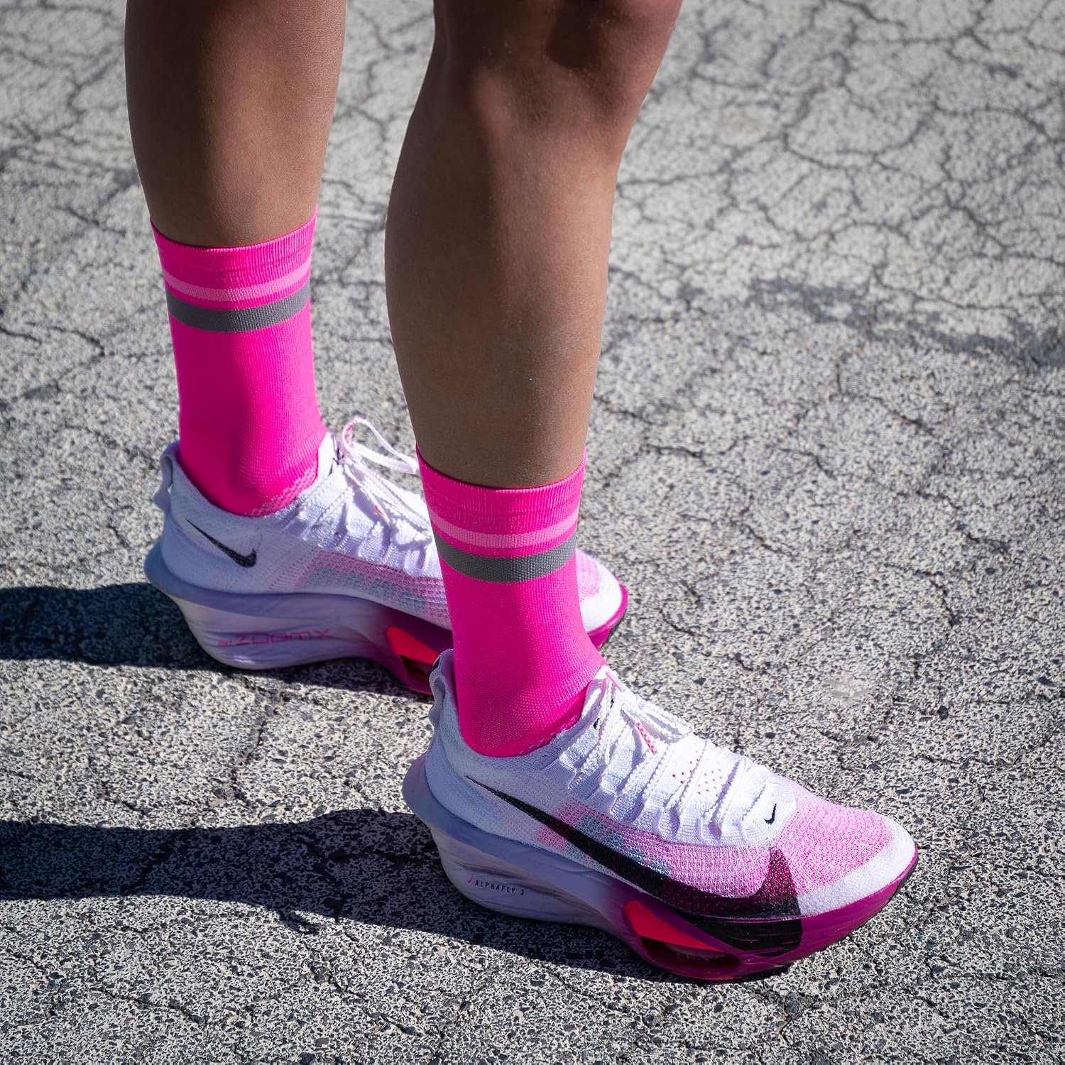 Calze da corsa NORTEI rosa fluo ai piedi di un runner su asfalto