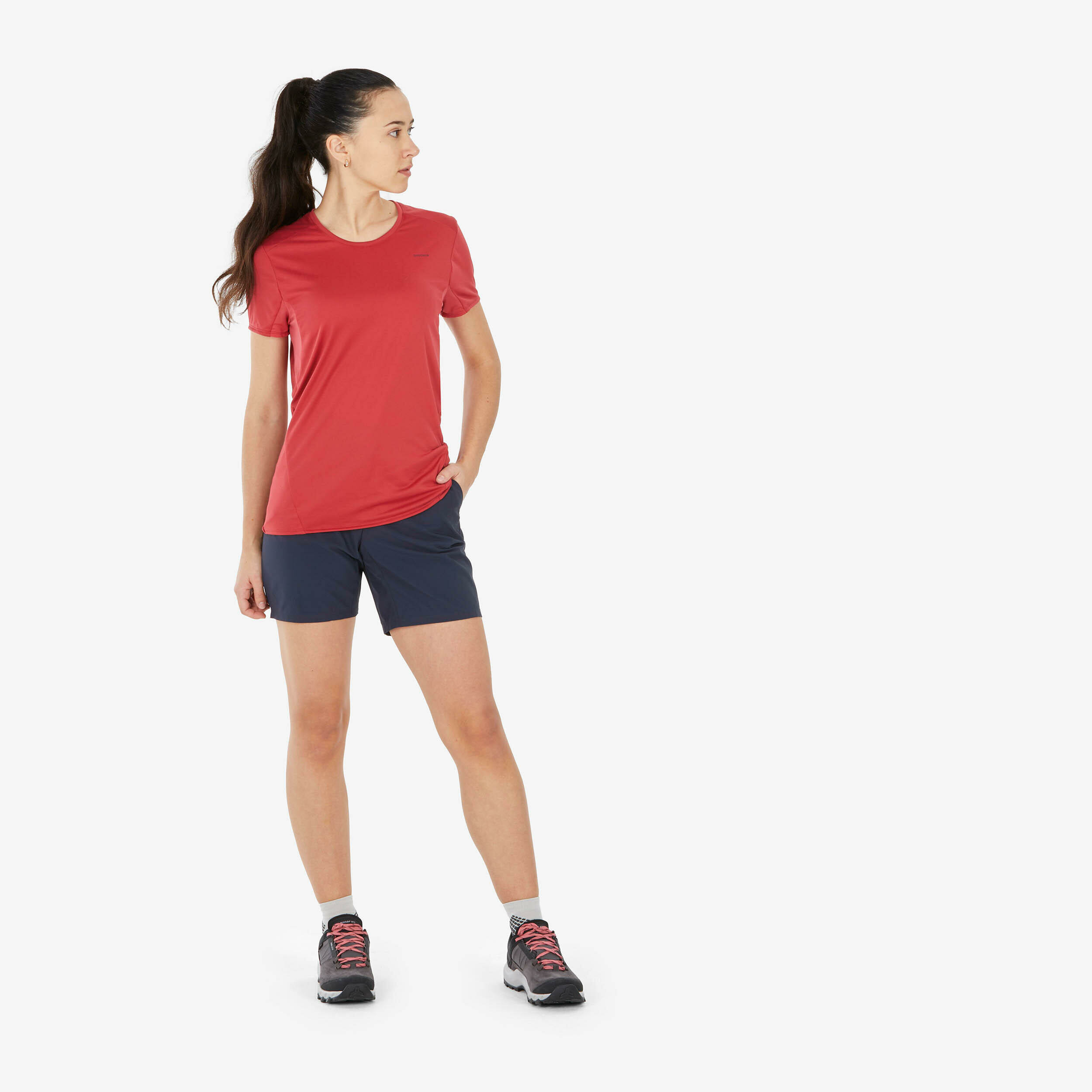 Escursionista in maglietta rossa e pantaloncini blu con le scarpe Quechua MH500 Low ai piedi