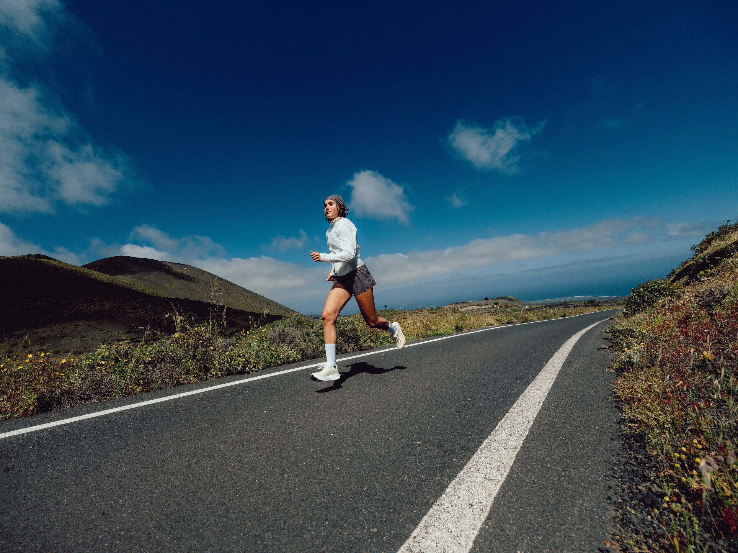 Runner che corre su una strada asfaltata tra colline sotto un cielo blu