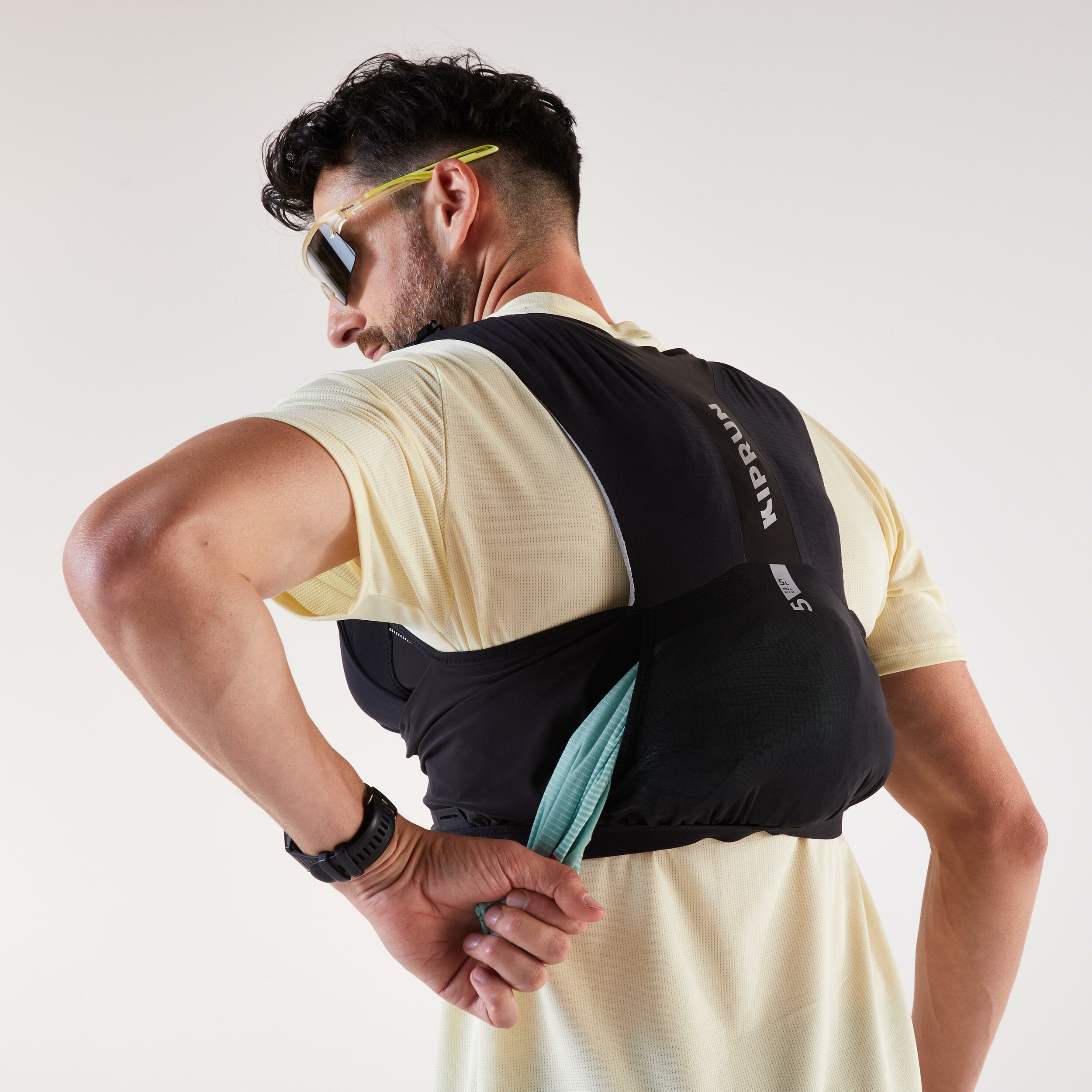 Runner che prende qualcosa dalla tasca a marsupio dietro il gilet Kiprun 900 Race