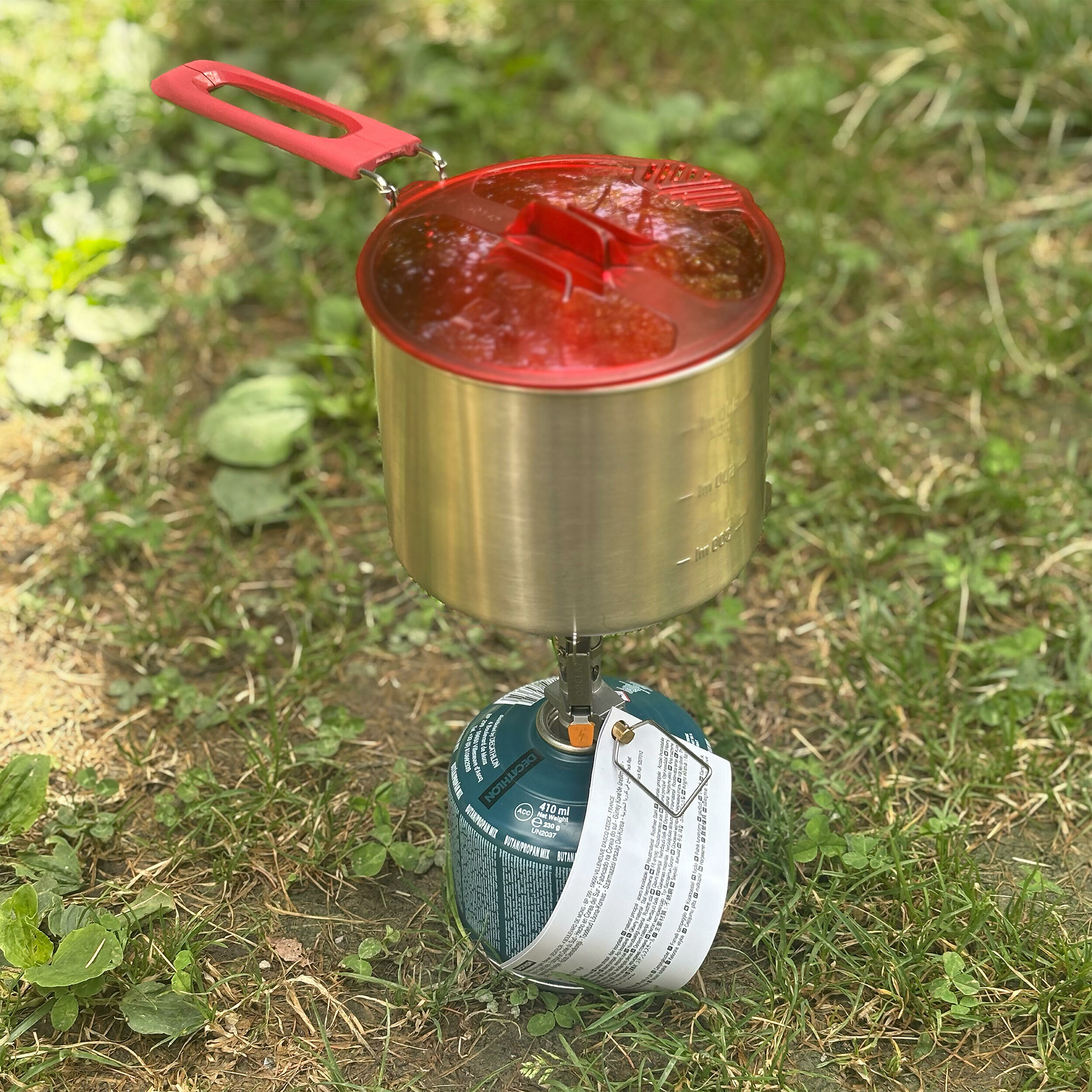 Fornellino Forclaz MT500 Compact avvitato su una cartuccia di gas con una pentola sopra, appoggiato sullerba