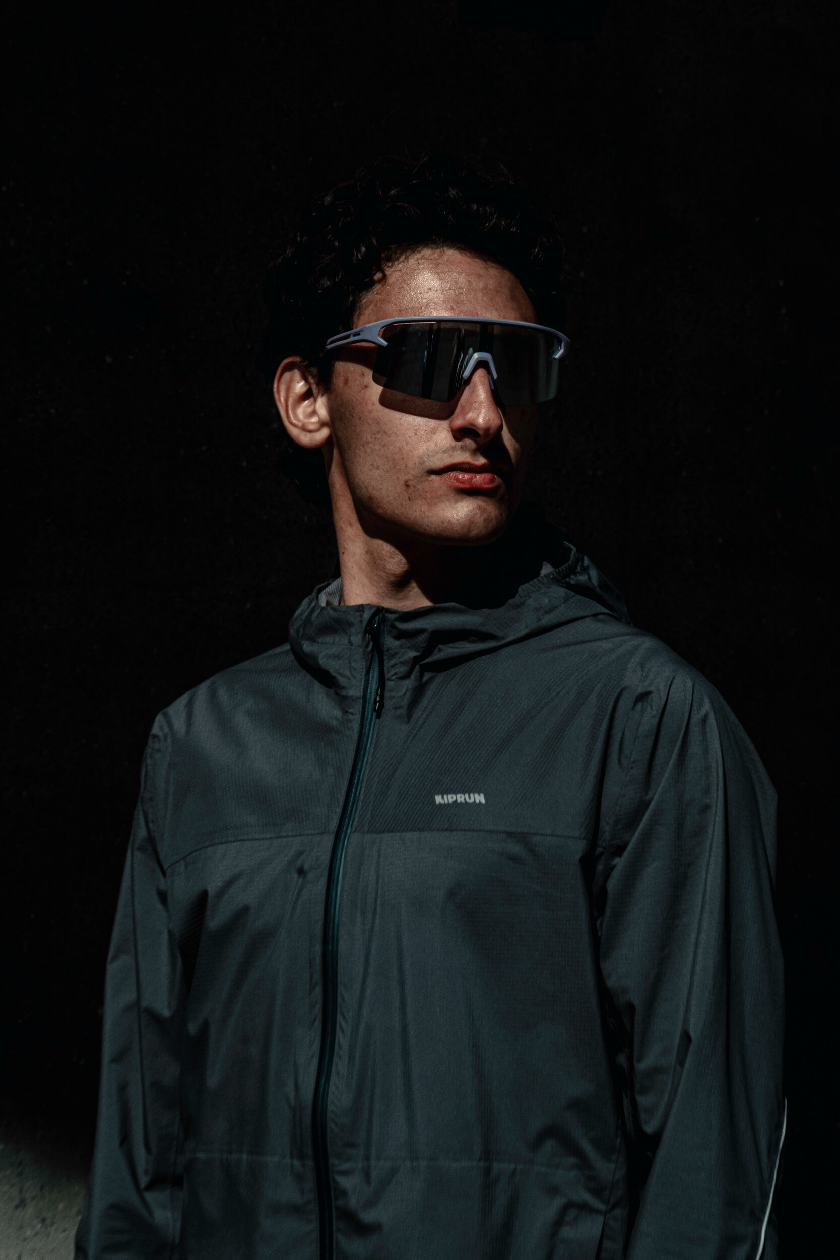 Runner con occhiali sportivi e giacca Kiprun Run Flow su sfondo scuro