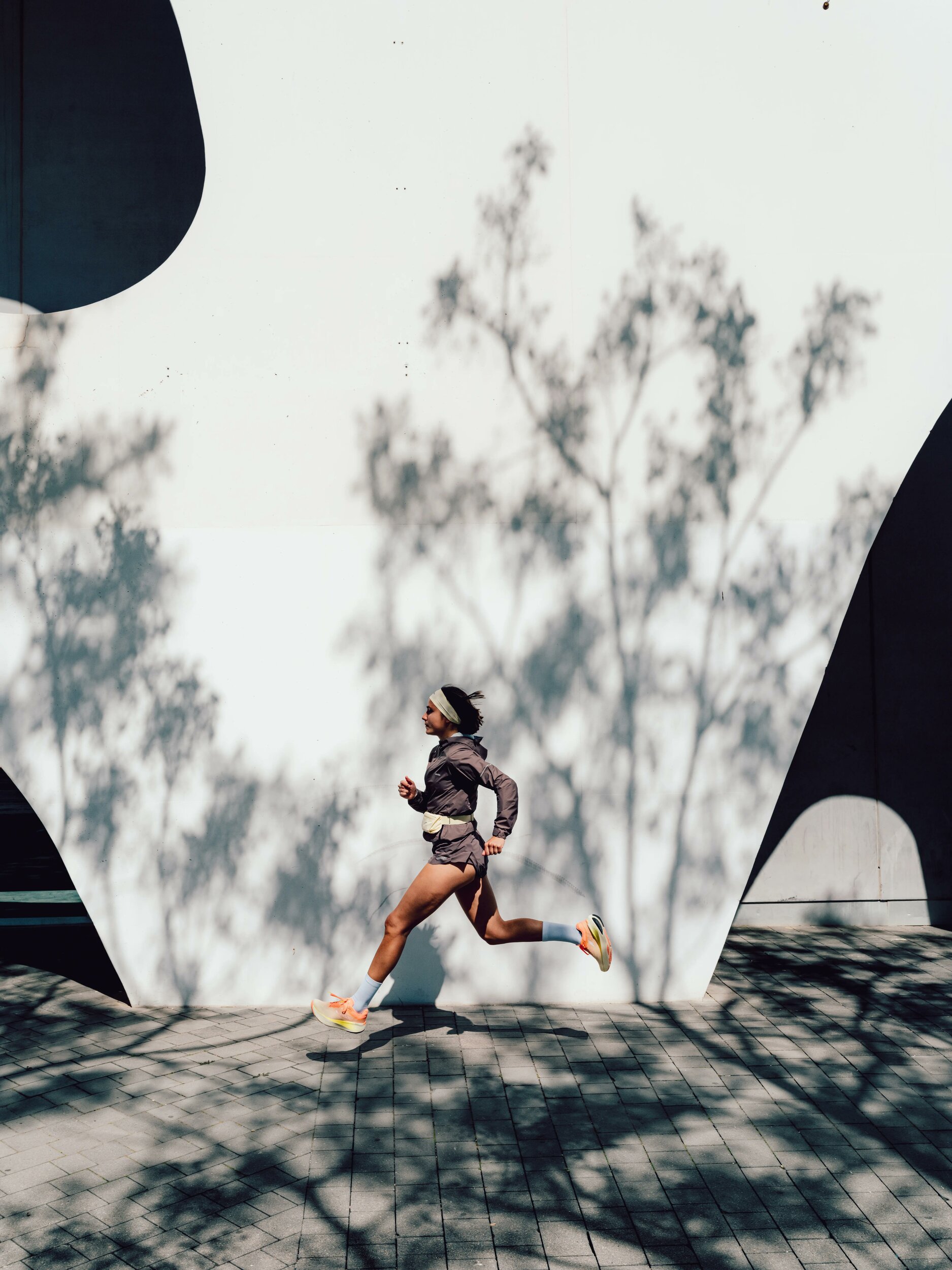Runner che corre davanti a un muro bianco con la giacca Kiprun Run Rain 900 marrone