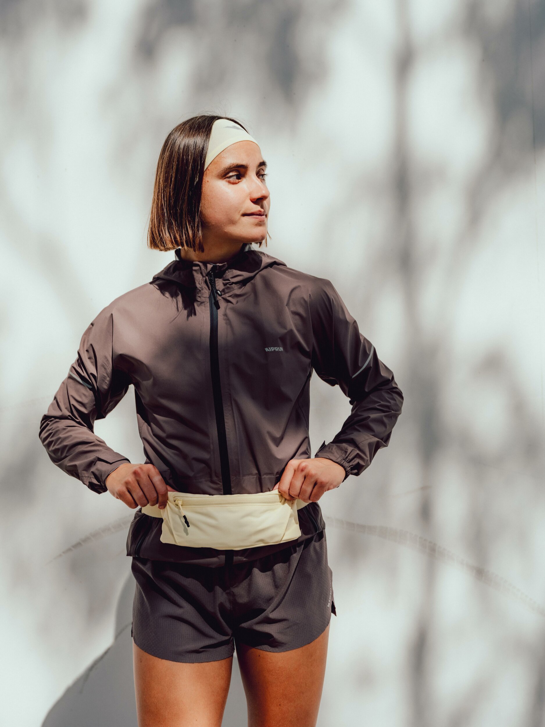 Runner con giacca Kiprun Run Rain 900 aperta e marsupio da corsa in vita