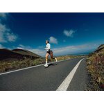 Runner che corre su una strada asfaltata tra colline sotto un cielo blu
