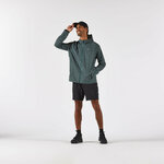 Runner in piedi con giacca Kiprun Run Flow verde militare, pantaloncini neri e cappellino