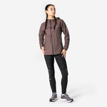Donna in piedi con giacca Kiprun Run Rain 900 marrone, leggings neri e scarpe da corsa