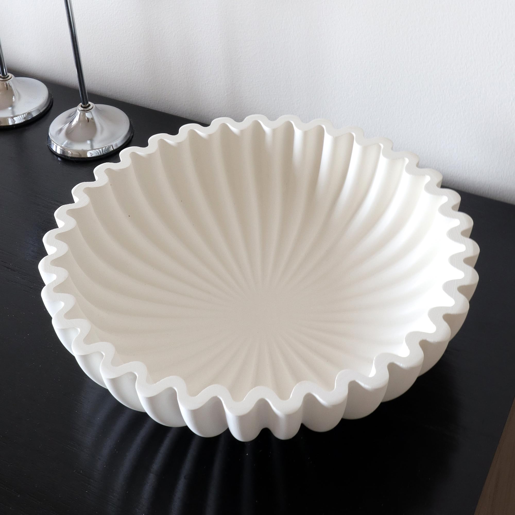 Weiße Plissee-Schale aus Beton mit gewelltem Rand auf einem schwarzen Sideboard
