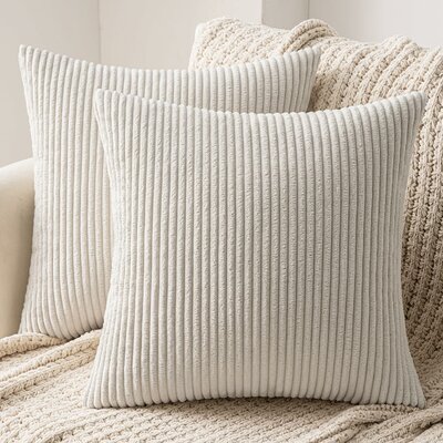 Zwei beige Cordkissen mit Längsrippen auf einem hellen Sofa vor einer Strickdecke