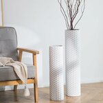 Zwei weiße Metallvasen mit Wabenmuster, 70 und 55 cm, mit dunklen Zweigen neben einem grauen Sessel