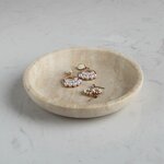 Runde beige Travertinschale mit Ohrringen auf heller Marmorfläche