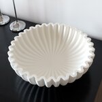 Weiße Plissee-Schale aus Beton mit gewelltem Rand auf einem schwarzen Sideboard
